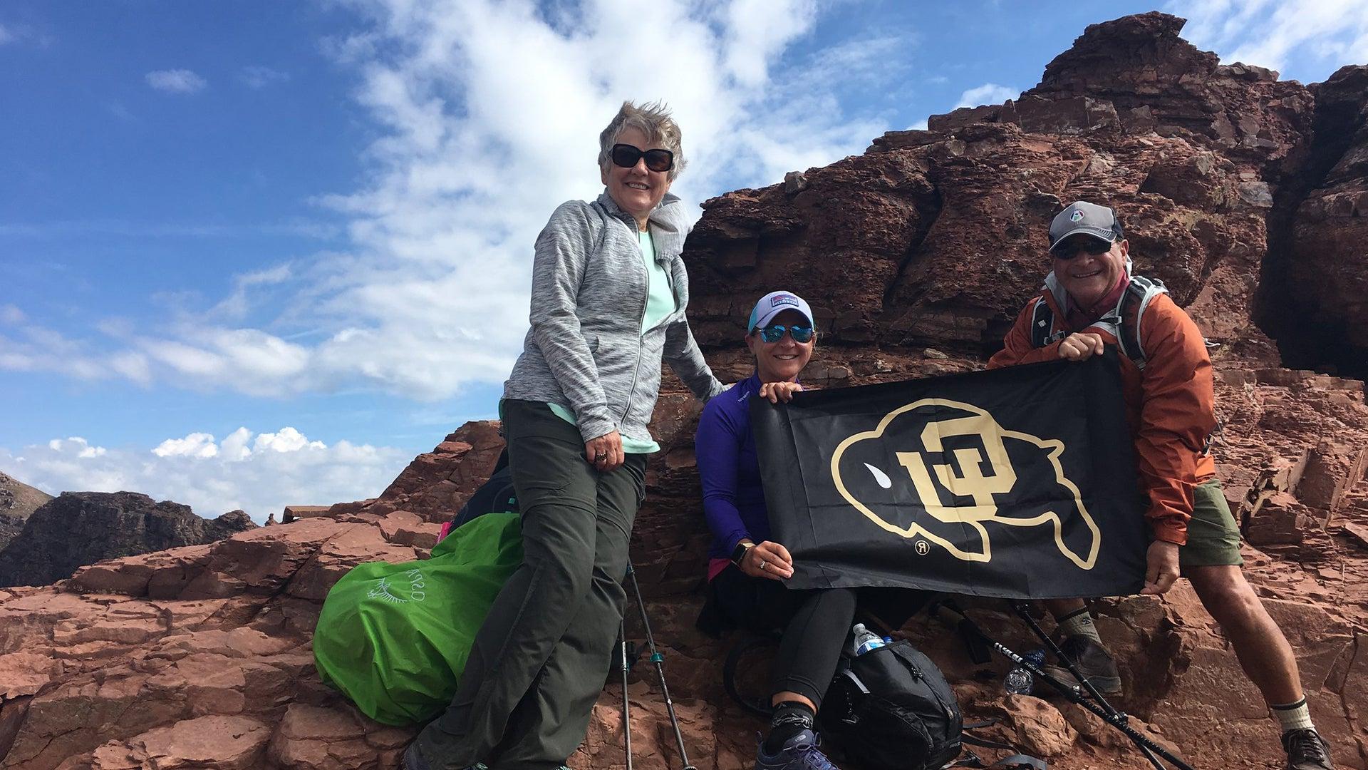 A group of alumni with a CU Bouder flag on a mountaintop