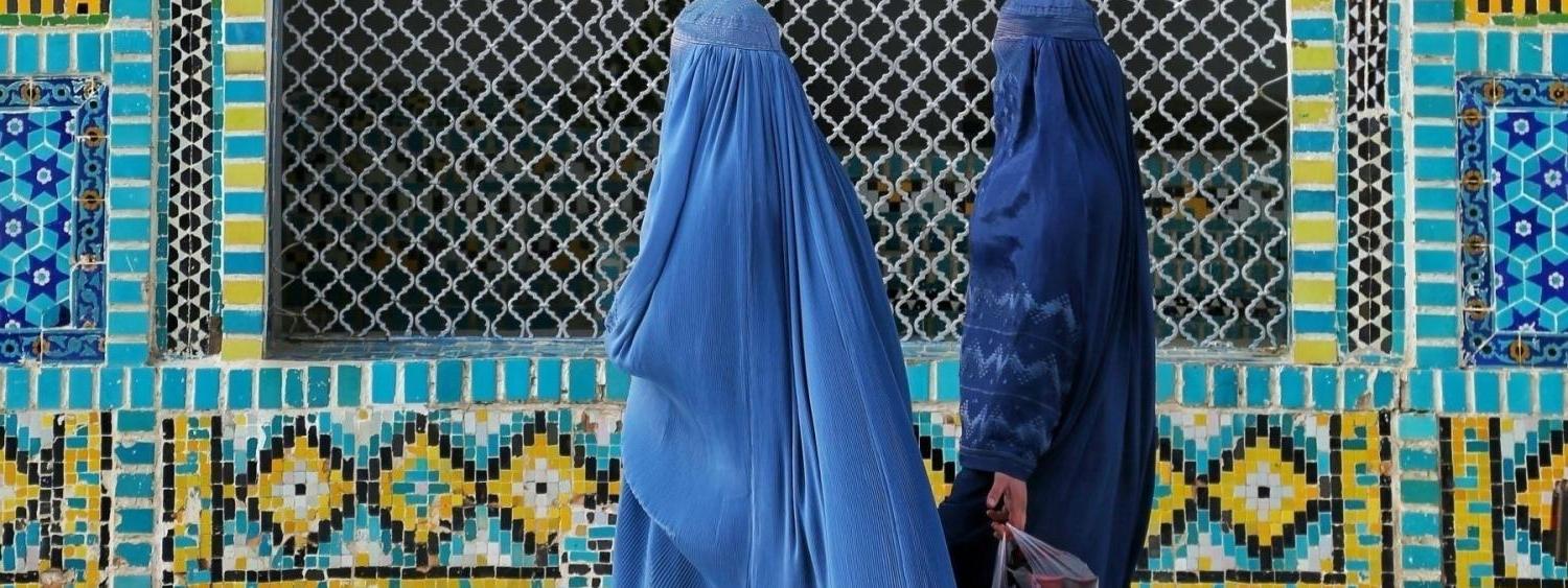 women in blue burqas walking past a colorfully tiled wall