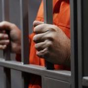 Man in orange jumpsuit holding prison bars