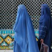 women in blue burqas walking past a colorfully tiled wall