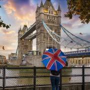 一位游客在伦敦塔桥前，拿着一把英国国旗的雨伞.