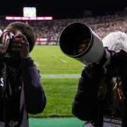 Two students take photos of the crowd during a home football game. 