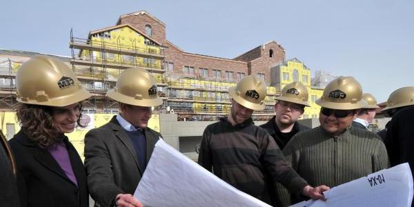 A group of construction engineers looks at blueprints outside a campus building under construction