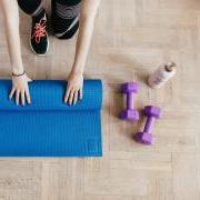 Person rolling up a yoga mat on the floor next to a water bottle and two dumbbells.