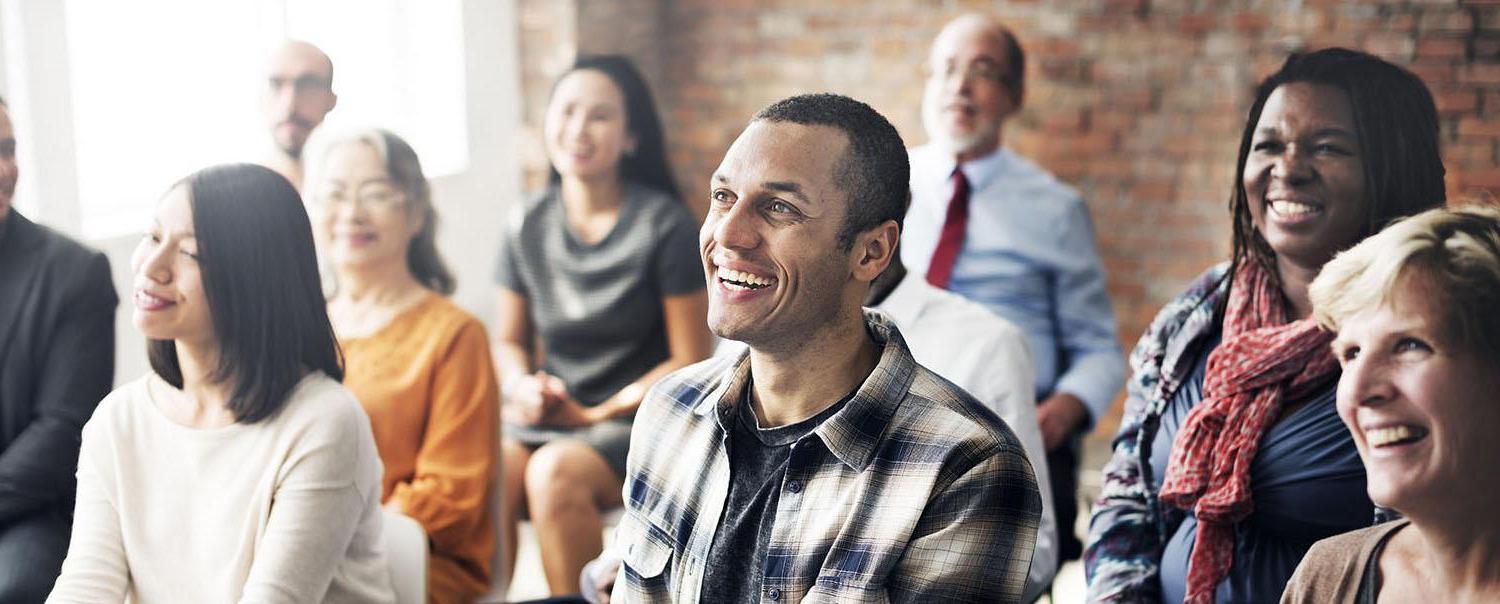 Group of people in a seminar setting sitting down and smiling.