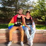 Students sitting outdoors on campus with a pride flag draped around their shoulders